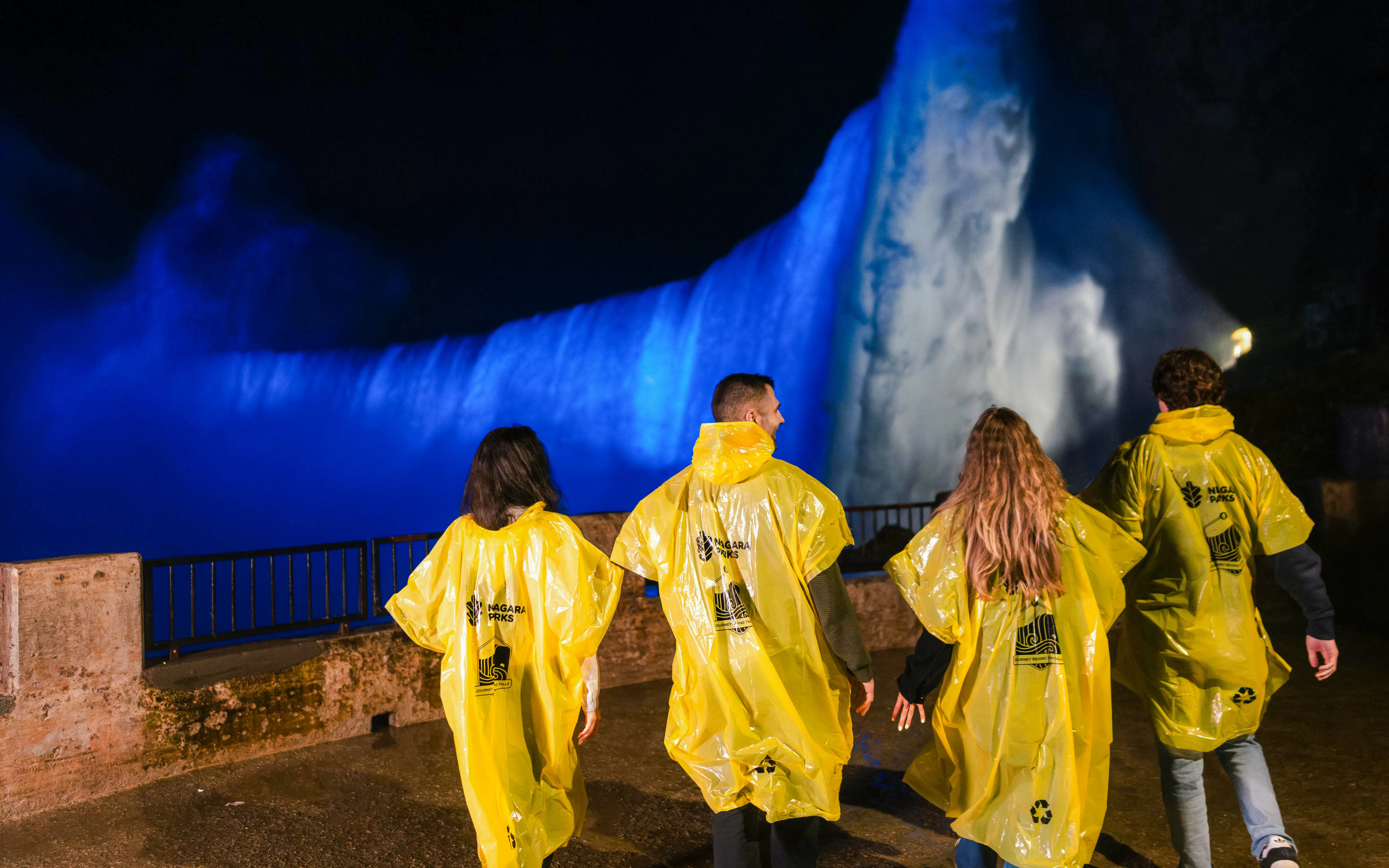Visitors in yellow ponchos view illuminated Niagara Falls at night during Journey Behind the Falls tour.