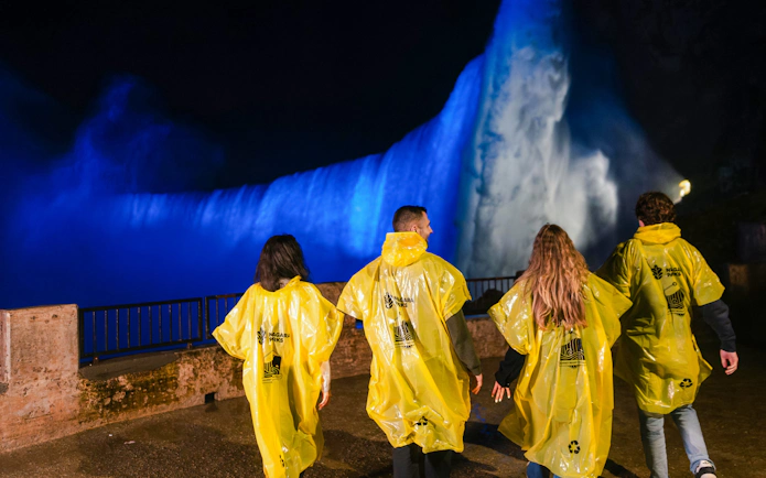 Visitors in yellow ponchos view illuminated Niagara Falls at night during Journey Behind the Falls tour.