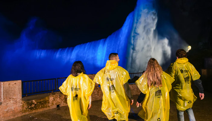 Visitors in yellow ponchos view illuminated Niagara Falls at night during Journey Behind the Falls tour.