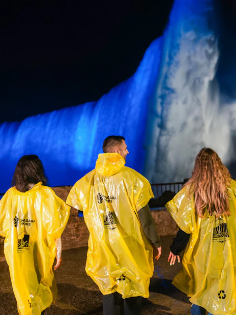 Visitors in yellow ponchos view illuminated Niagara Falls at night during Journey Behind the Falls tour.