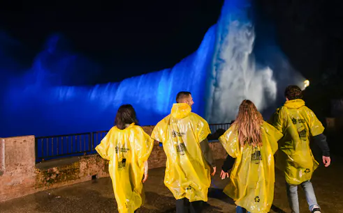 Visitors in yellow ponchos view illuminated Niagara Falls at night during Journey Behind the Falls tour.