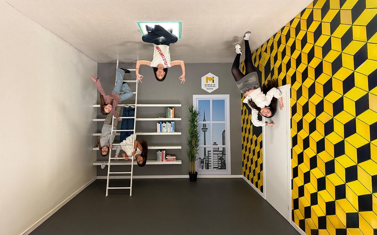 Visitors interacting with an upside-down room exhibit at the Museum of Illusions in Madrid.