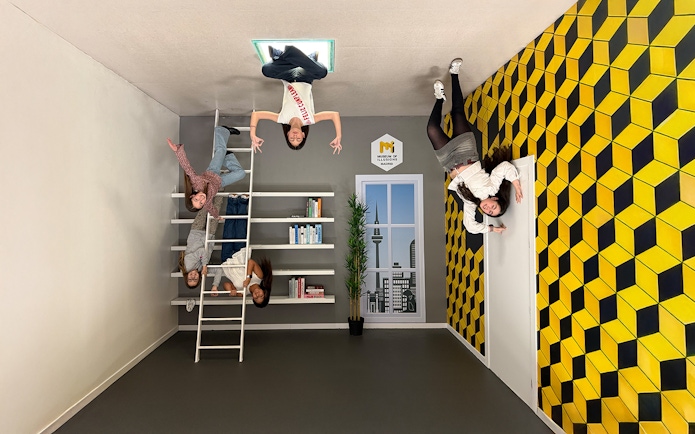 Visitors interacting with an upside-down room exhibit at the Museum of Illusions in Madrid.
