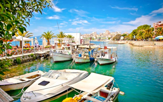 Boats docked at Saranda city port, Ionian Sea, Albania, with waterfront cafes and palm trees.