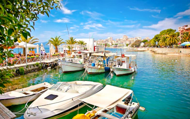 Boats docked at Saranda city port, Ionian Sea, Albania, with waterfront cafes and palm trees.