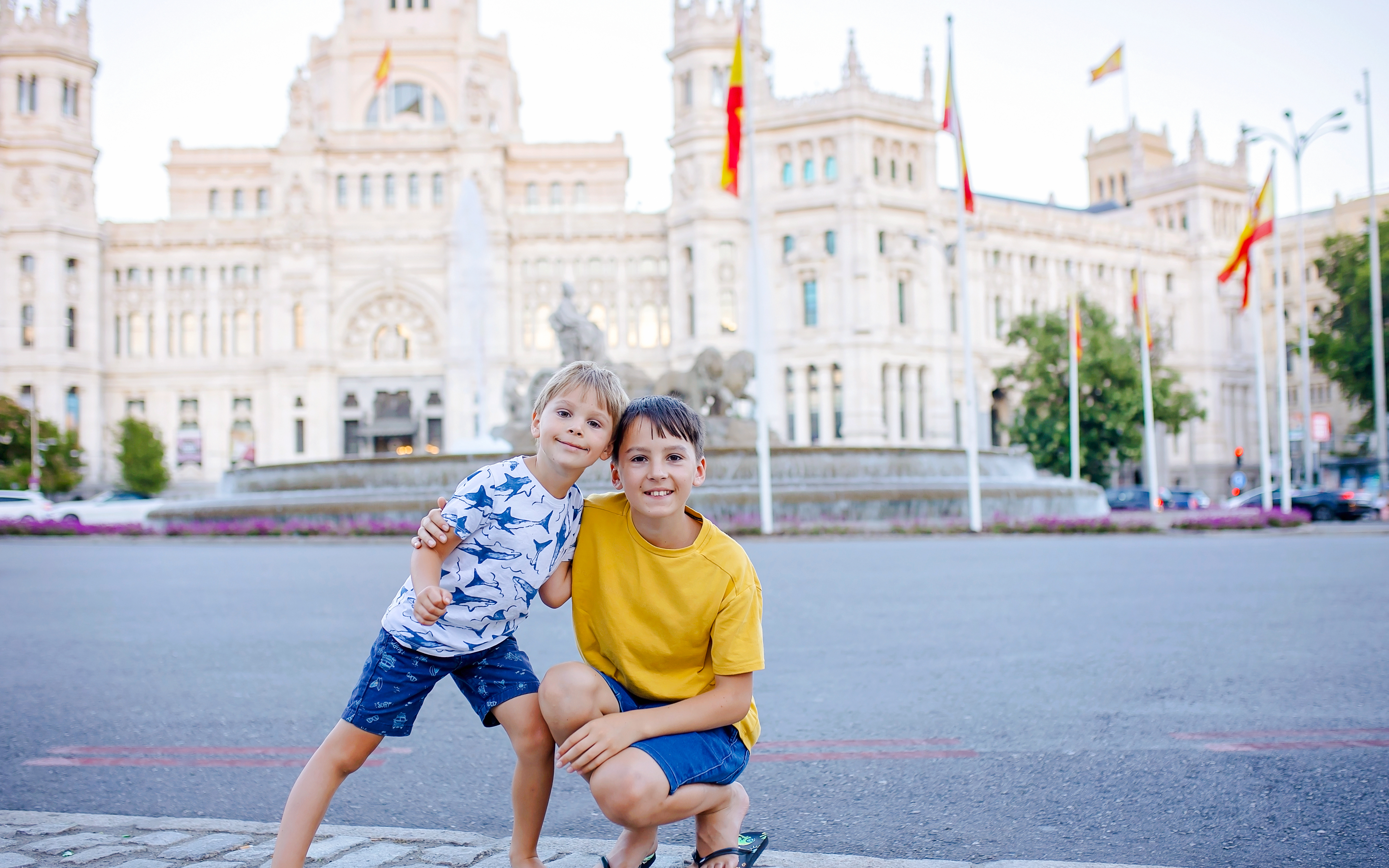 Two boys in front of Cibeles Fountain and Cibeles Palace, Madrid.