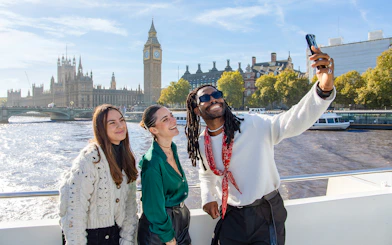 Friends taking a selfie on a Thames River cruise with Big Ben in the background, London.