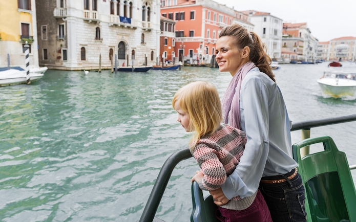 Mother and daughter on Venice water bus with cityscape in background.