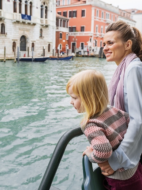 Mother and daughter on Venice water bus with cityscape in background.