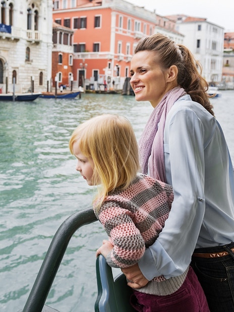 Mother and daughter on Venice water bus with cityscape in background.