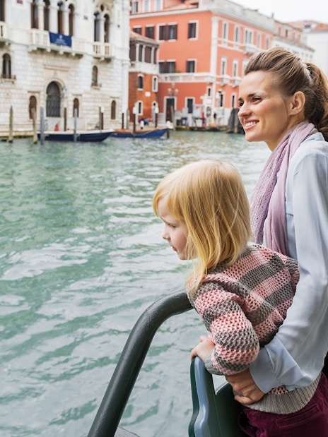Mother and daughter on Venice water bus with cityscape in background.