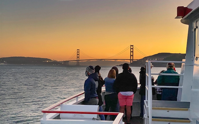Guests on deck viewing Golden Gate Bridge during California sunset cruise.
