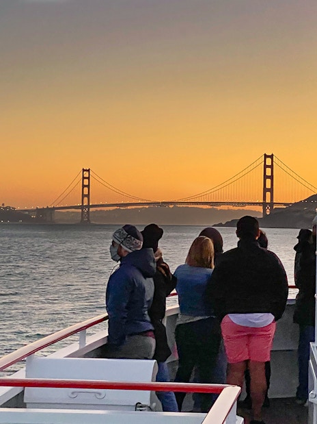 Guests on deck viewing Golden Gate Bridge during California sunset cruise.