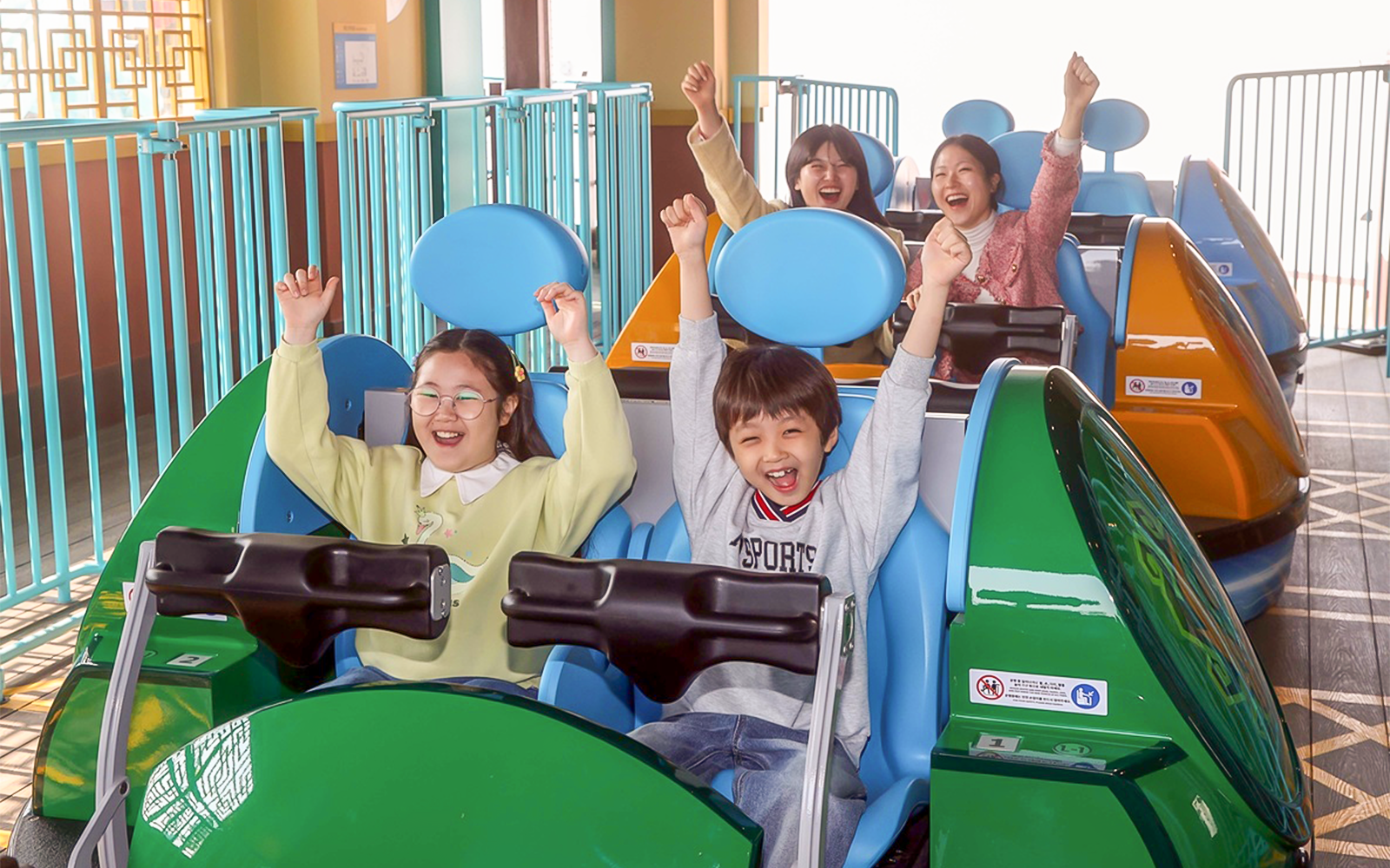 Kids enjoying a theme park ride with arms raised in excitement.