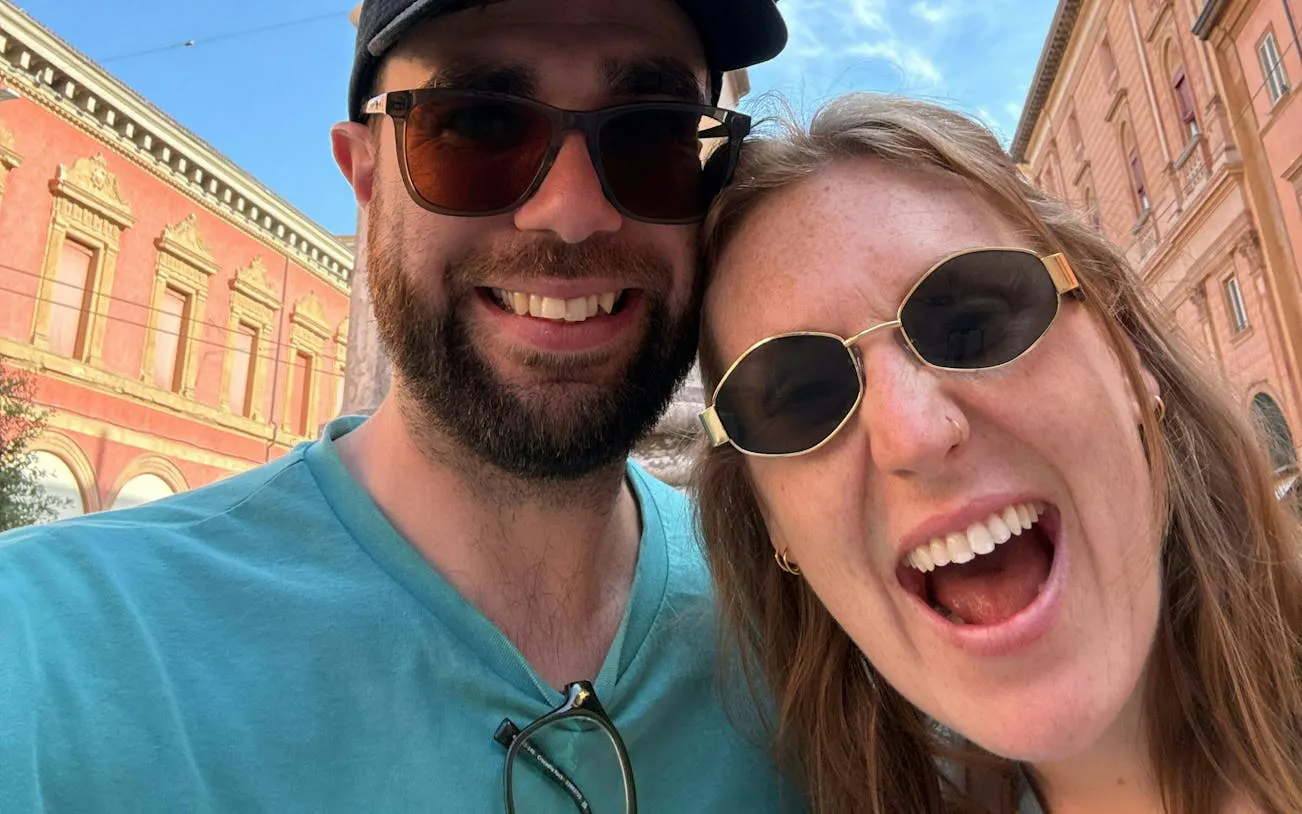 Couple enjoying a sunny day in Bologna with historic buildings in the background.