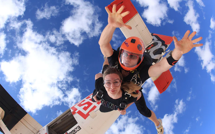Tandem skydivers freefalling over Dubai's Palm Drop Zone with blue sky backdrop.