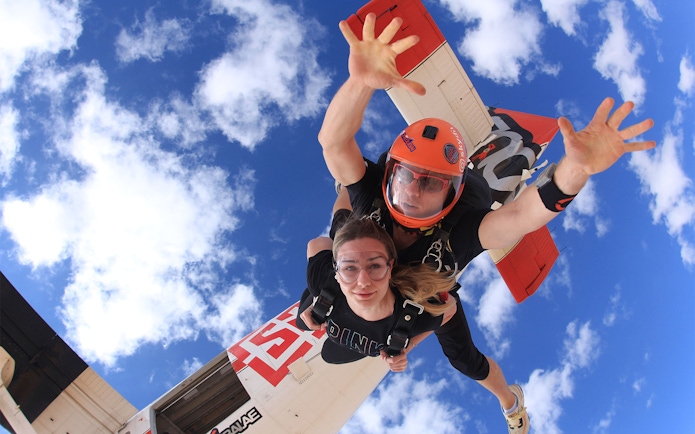 Tandem skydivers freefalling over Dubai's Palm Drop Zone with blue sky backdrop.