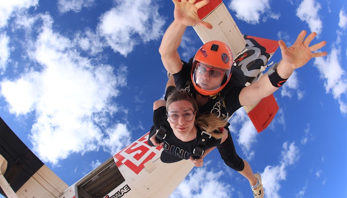 Tandem skydivers freefalling over Dubai's Palm Drop Zone with blue sky backdrop.