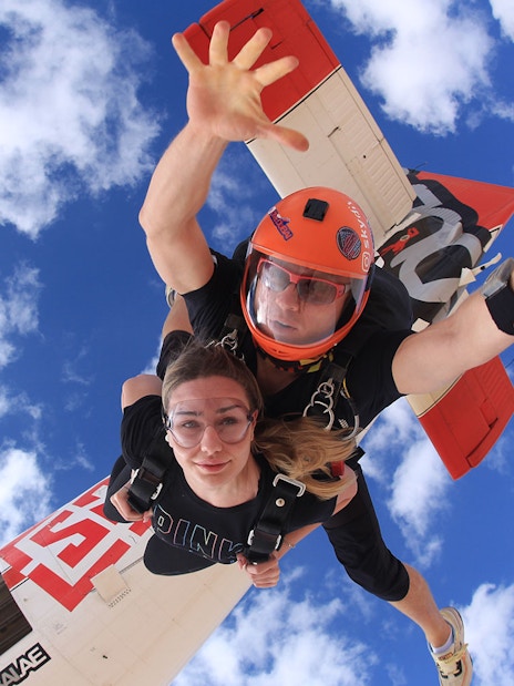 Tandem skydivers freefalling over Dubai's Palm Drop Zone with blue sky backdrop.