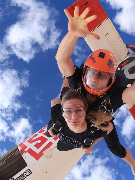 Tandem skydivers freefalling over Dubai's Palm Drop Zone with blue sky backdrop.
