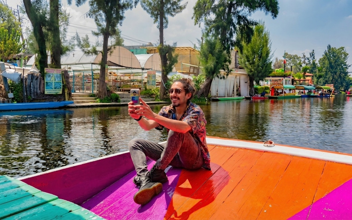 Person taking a selfie on a colorful boat in Xochimilco canals, Mexico City.