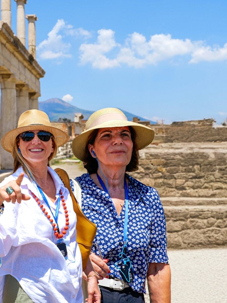 Female friends exploring ancient ruins at Pompeii with Mount Vesuvius in the background.