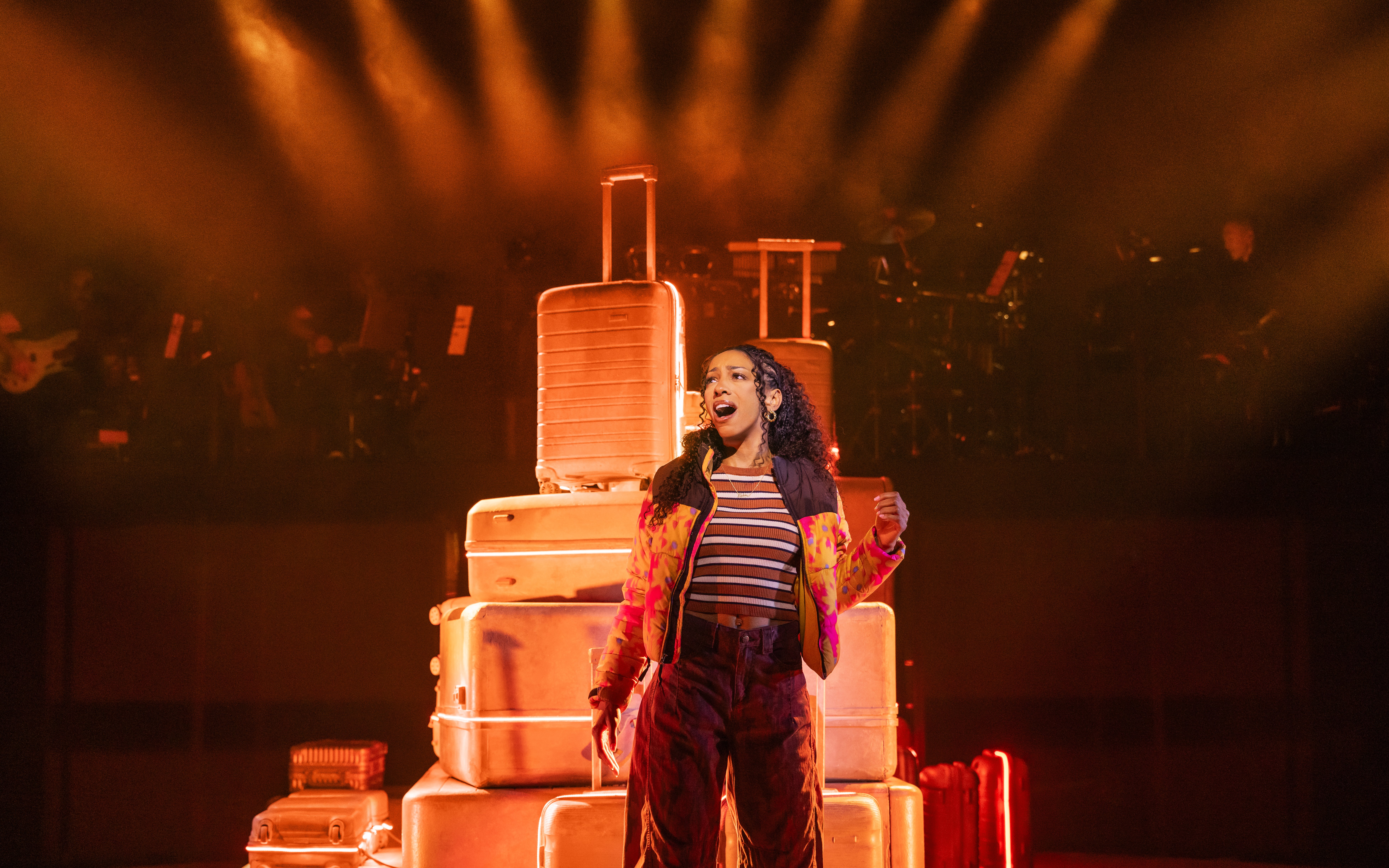 Performer singing on stage with stacked suitcases in "Two Strangers (Carry a Cake Across New York)" Broadway show.