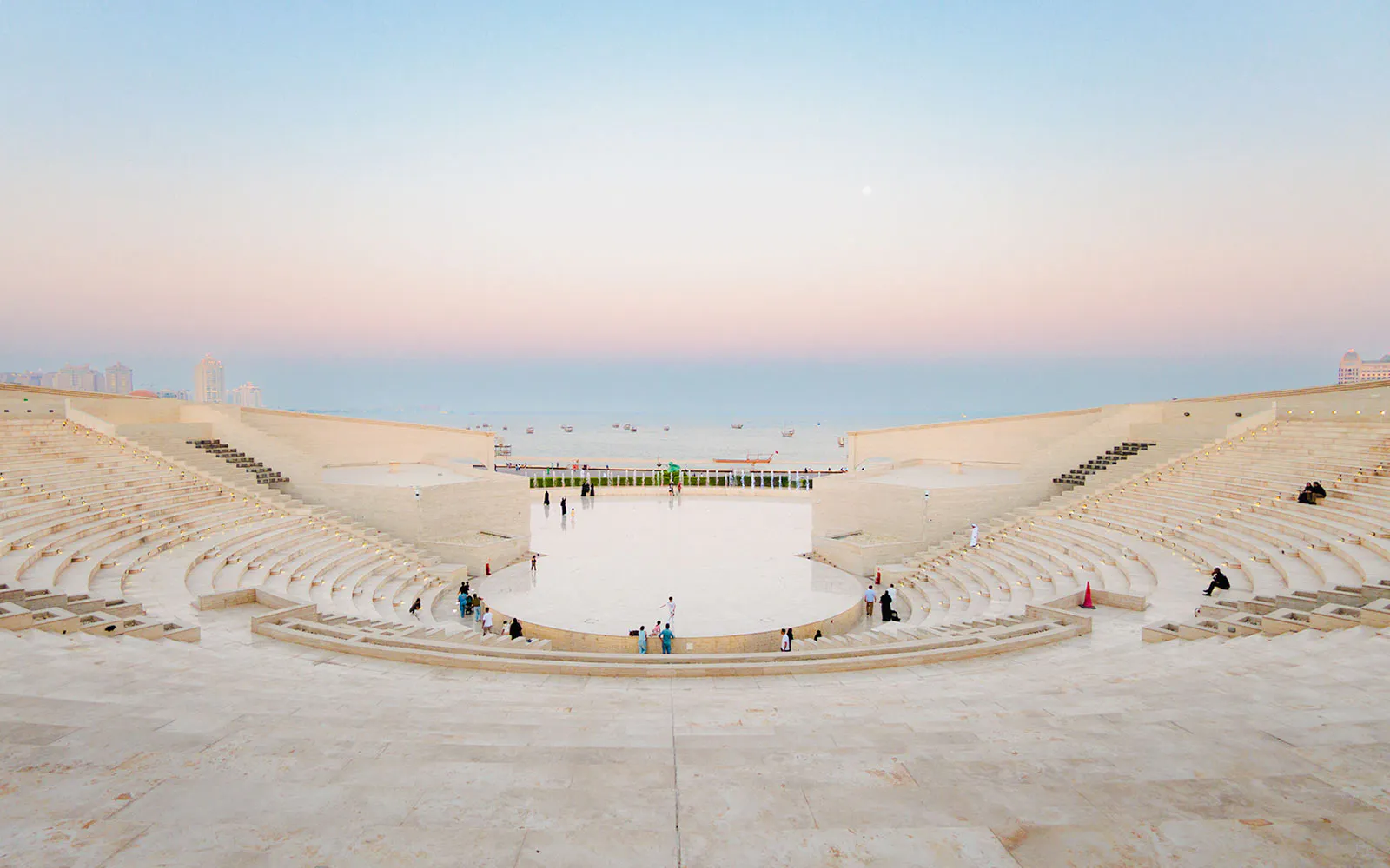 Amphitheater at Katara Village, Qatar, with people seated and sea view at sunset.