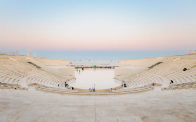 Amphitheater at Katara Village, Qatar, with people seated and sea view at sunset.