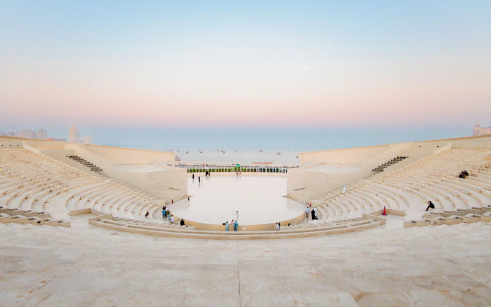 Amphitheater at Katara Village, Qatar, with people seated and sea view at sunset.