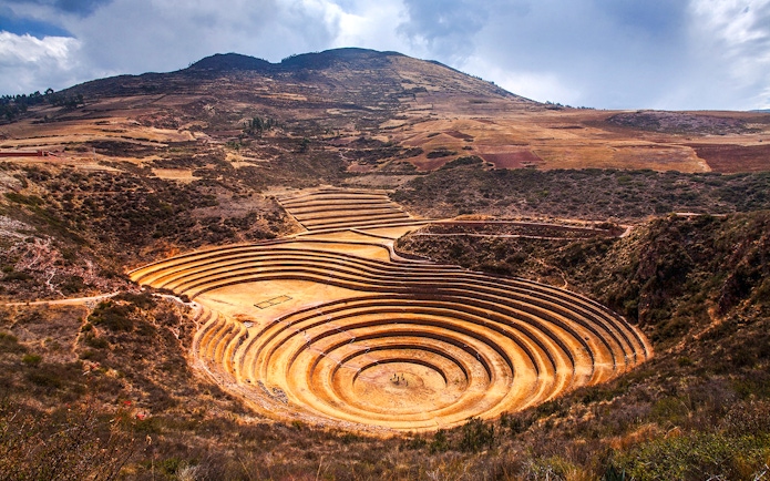 Moray archaeological site in Peru with circular terraces against a mountainous backdrop.