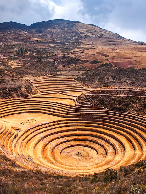 Moray archaeological site in Peru with circular terraces against a mountainous backdrop.