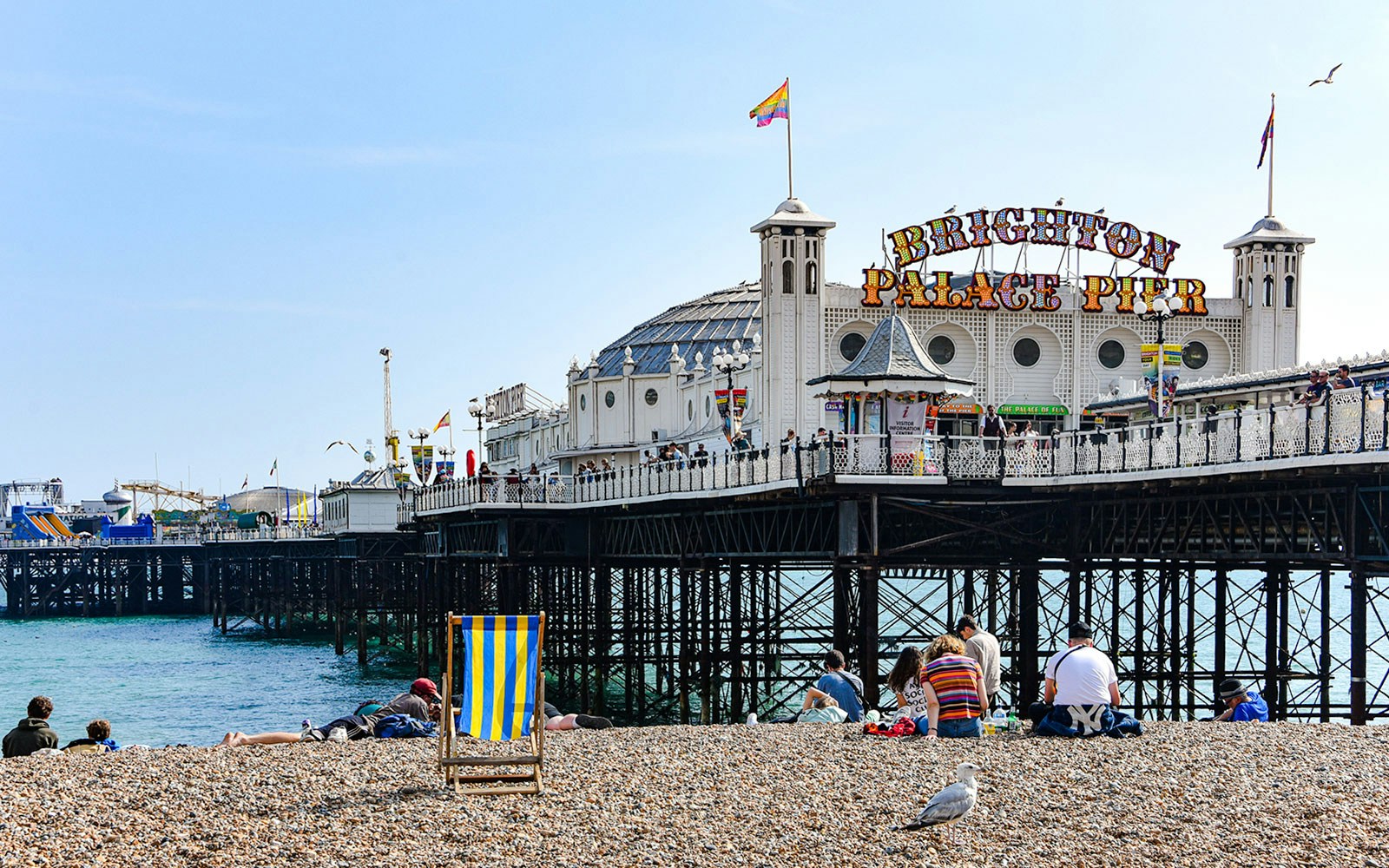 Brighton Pier with people relaxing on the pebble beach in the afternoon.