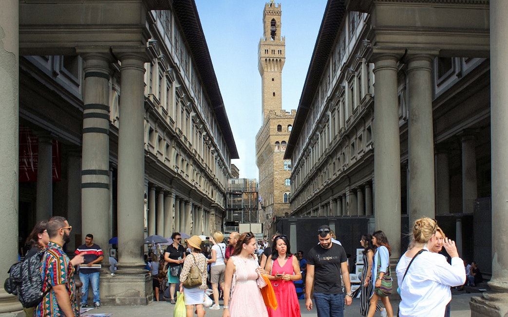 Visitors walking through the Uffizi Gallery courtyard in Florence, Italy, with Palazzo Vecchio in the background.