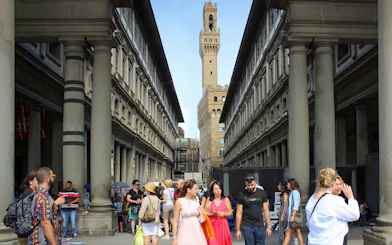 Visitors walking through the Uffizi Gallery courtyard in Florence, Italy, with Palazzo Vecchio in the background.