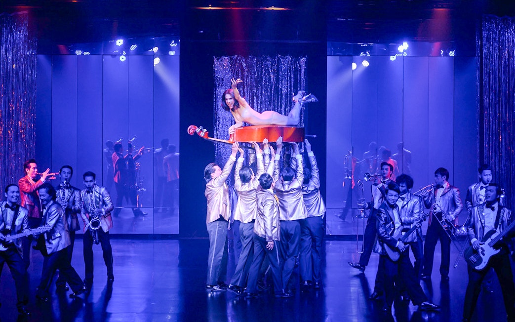 Performer on cello held by dancers at Calypso Cabaret, Bangkok.