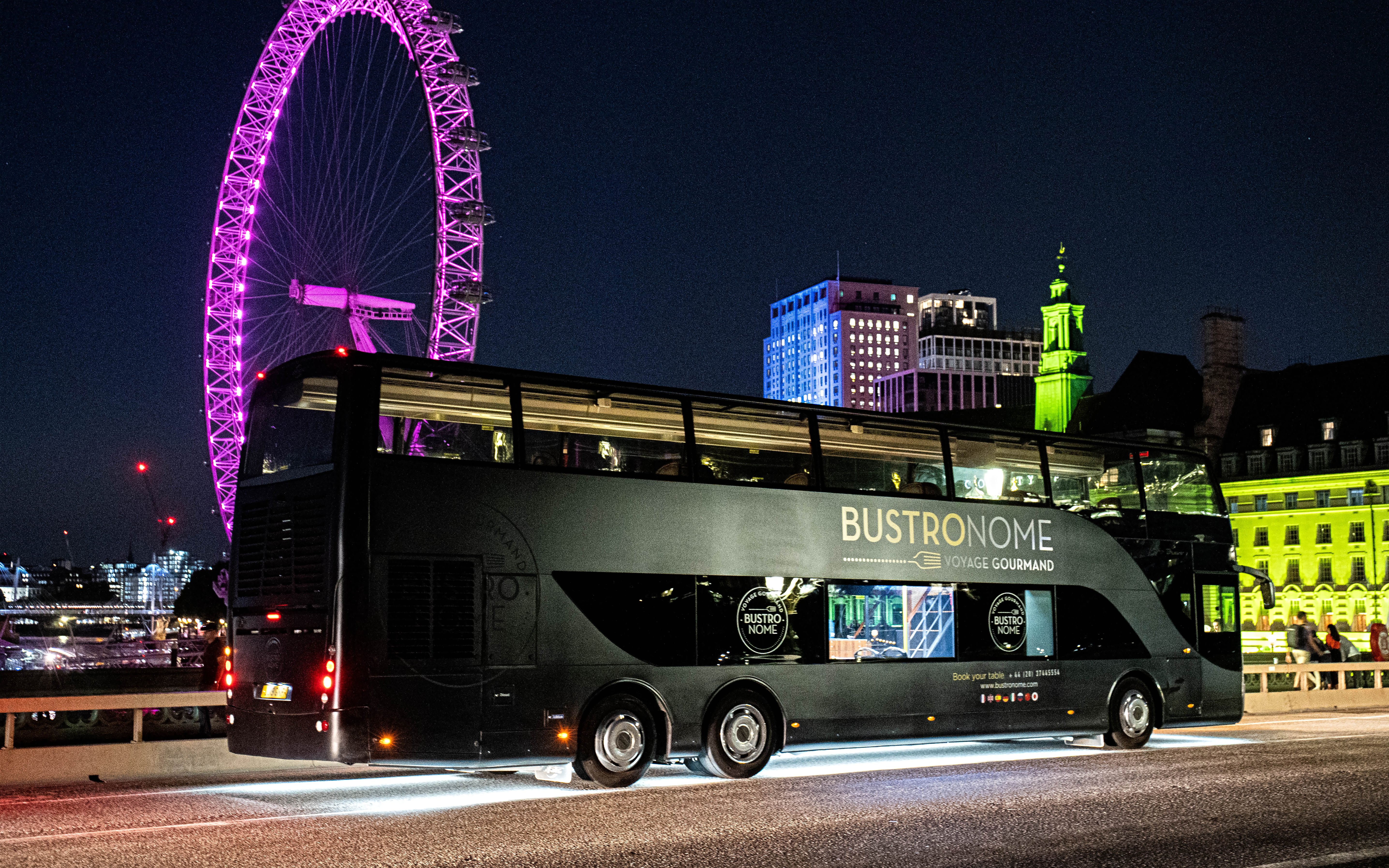 Bustronome bus at night with London Eye illuminated in the background.