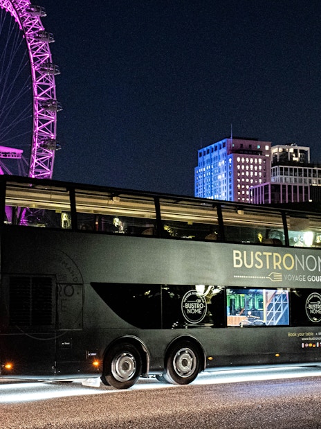 Bustronome bus at night with London Eye illuminated in the background.