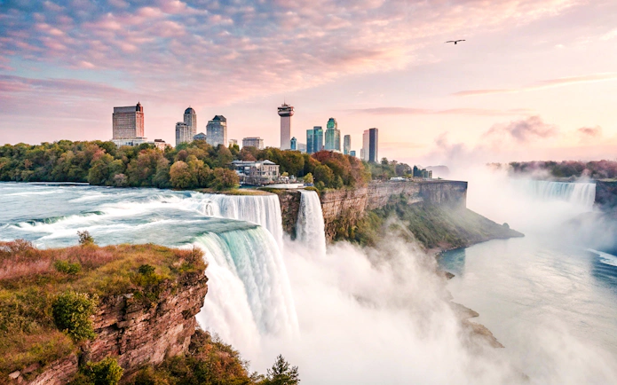 Niagara Falls with city skyline in the background at sunrise, USA.