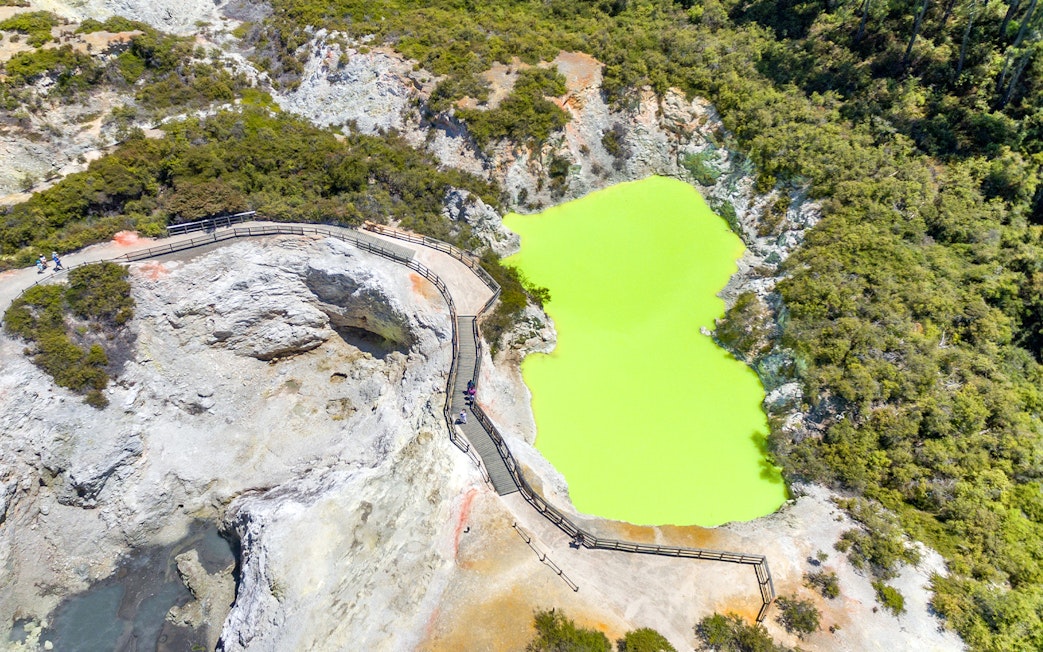 Aerial view of a vibrant green geothermal pool with a boardwalk in Rotorua, Auckland.