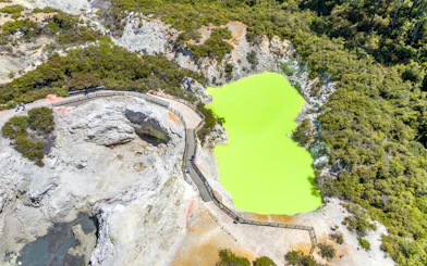 Aerial view of a vibrant green geothermal pool with a boardwalk in Rotorua, Auckland.