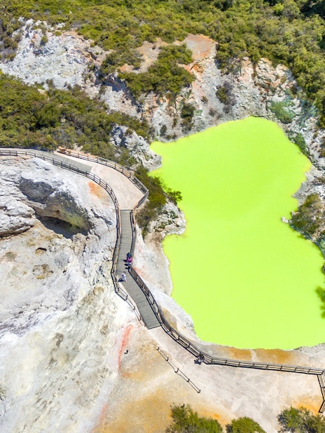 Aerial view of a vibrant green geothermal pool with a boardwalk in Rotorua, Auckland.