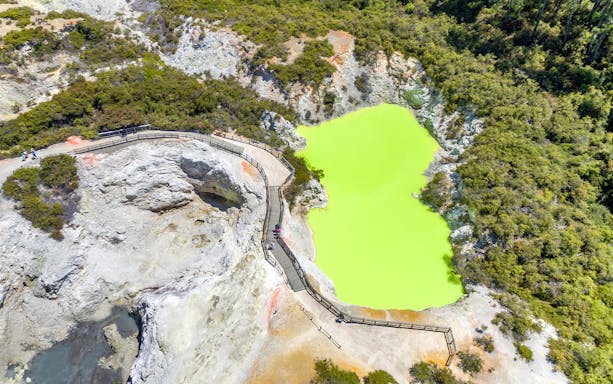Aerial view of a vibrant green geothermal pool with a boardwalk in Rotorua, Auckland.