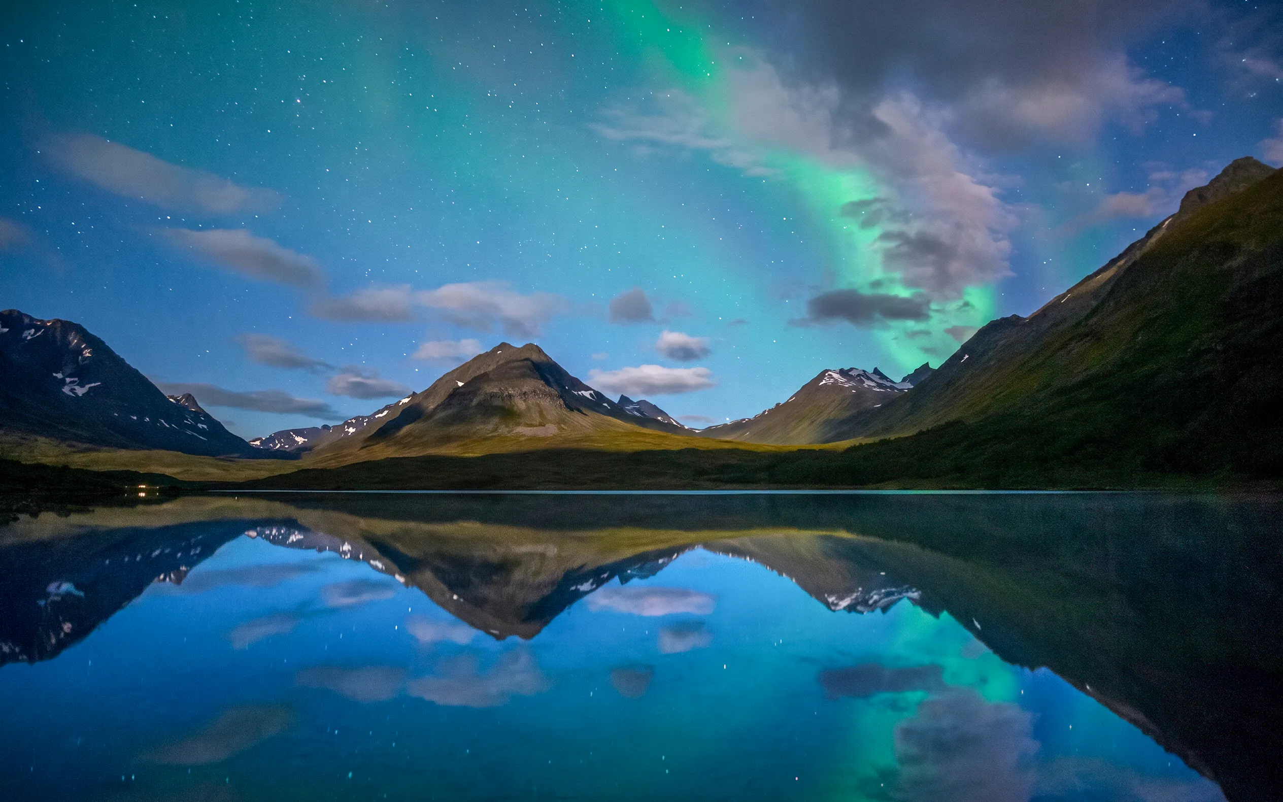Northern lights over Tromso mountains reflecting in a tranquil lake.