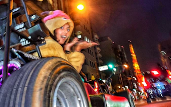 Go-karting tour participant in costume driving through Shibuya at night with Tokyo Tower in view.