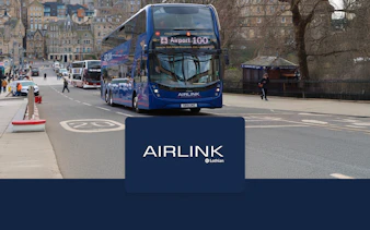 Edinburgh Airlink bus on city street near historic buildings.