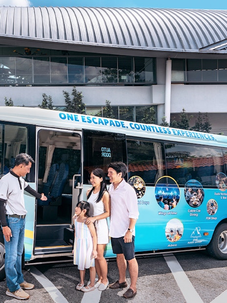 Family boarding a tour bus for Sentosa Island guided bus tour, with cable car station in background.