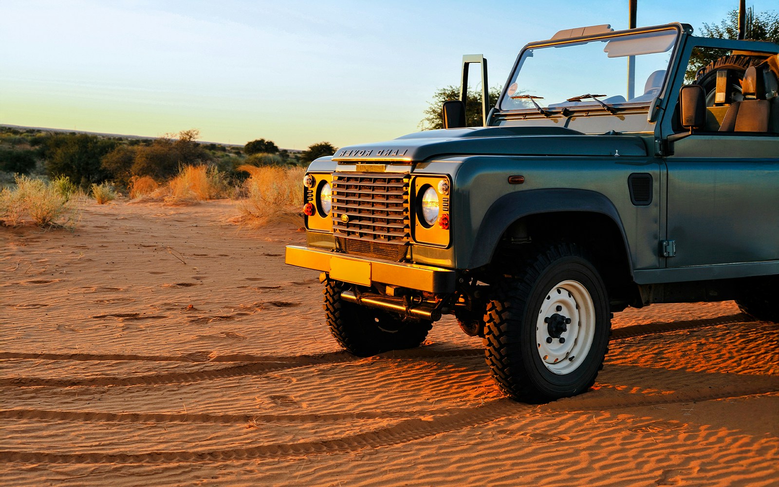 Old Land Rover parked on Dubai desert sand at sunset.