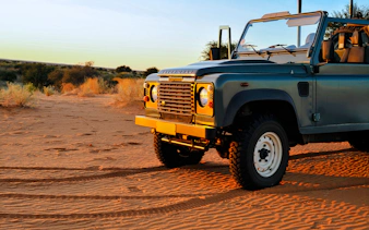 Old Land Rover parked on Dubai desert sand at sunset.