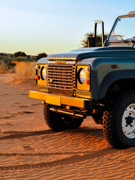 Old Land Rover parked on Dubai desert sand at sunset.